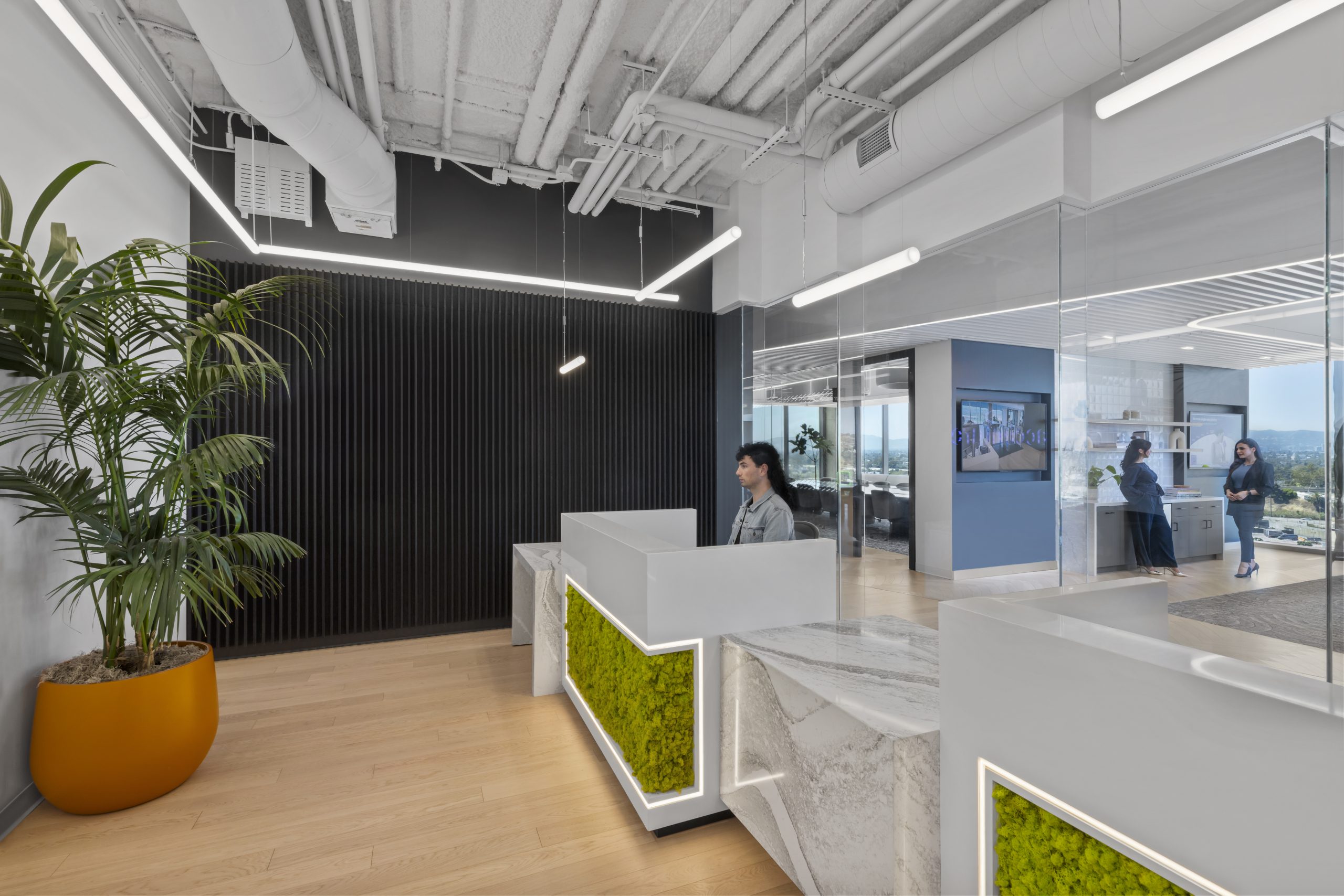 Modern office reception area at Accenture's Culver City office featuring custom reception desks, quartz countertops, integrated moss wall panels, LED lighting, and commercial millwork by DTANK+.